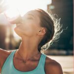 Sportlerin trinkt bei Sonnenuntergang aus einer Sportflasche – Symbolbild für vegane Trinkstrategie für Sportler:innen zur optimalen Flüssigkeitszufuhr beim Training.