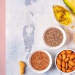 Lebensmittel mit hohem Omega-3-Gehalt wie Chiasamen, Leinsamen, Avocado, Walnüsse und Algenöl auf einem hellen Untergrund arrangiert.