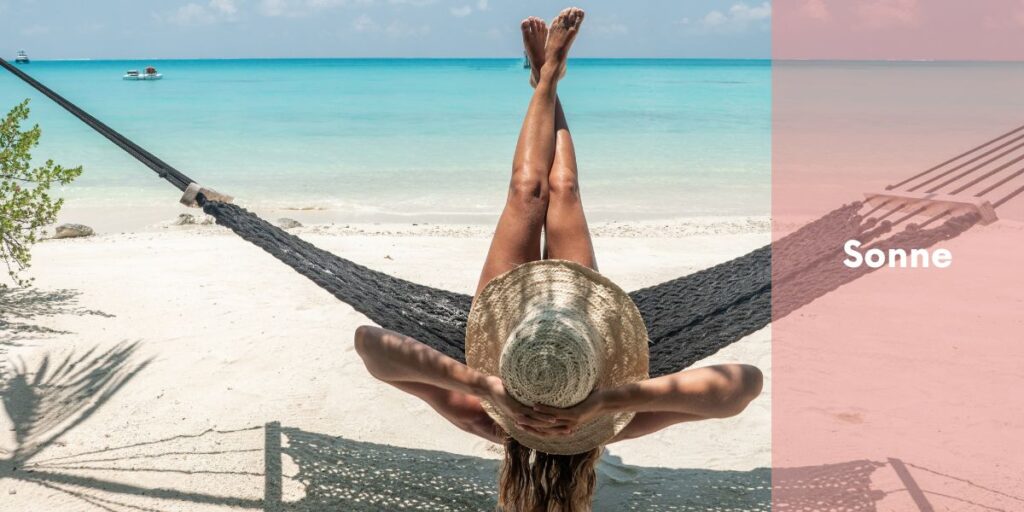 Eine Frau entspannt in einer Hängematte zwischen zwei Palmen und blickt auf das Meer. Sie trägt einen Strohhut und genießt die Sonne, was ihr hilft, die Eigenschutzzeit der Haut zu verlängern. Ihre überkreuzten Beine und die tropische Atmosphäre vermitteln Ruhe und Entspannung unter der Sonne.